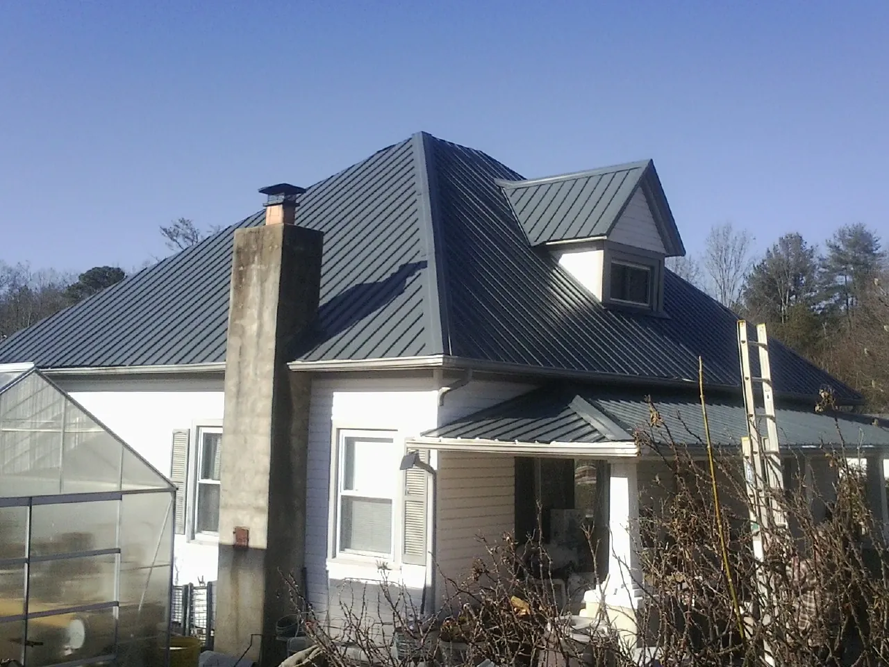 Dark blue standing seam metal roof on a white farmhouse with dormer — Slate & Tile Roof Repair by Roofing Brothers in Arnold