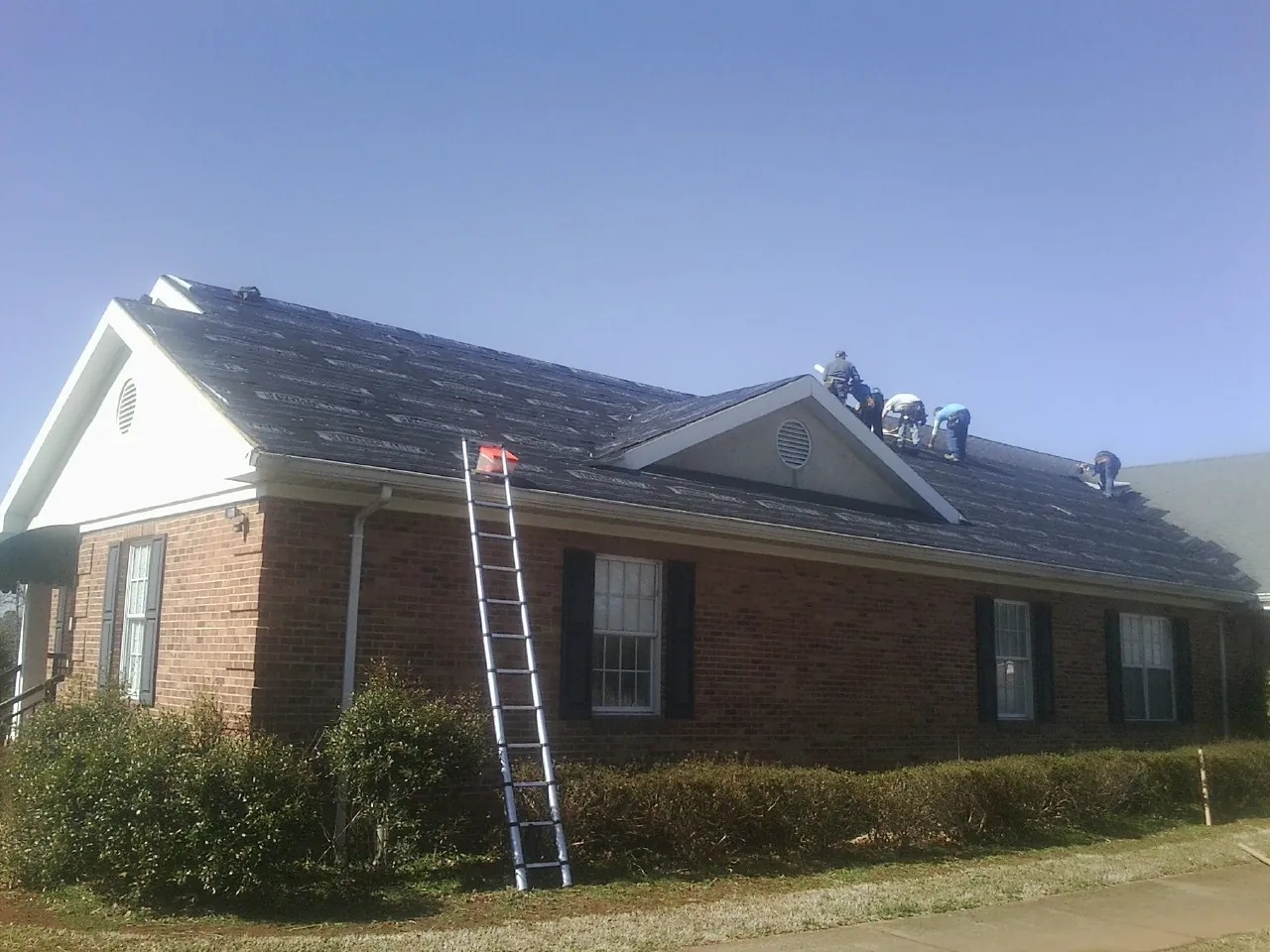 Crew tearing shingles off a brick ranch roof with a ladder set — Emergency Roof Repair work by our crew in Arnold