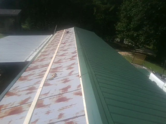 Old rusted panels beside newly installed green metal roofing — Wind Damage Roof Repair by Roofing Brothers in Arnold